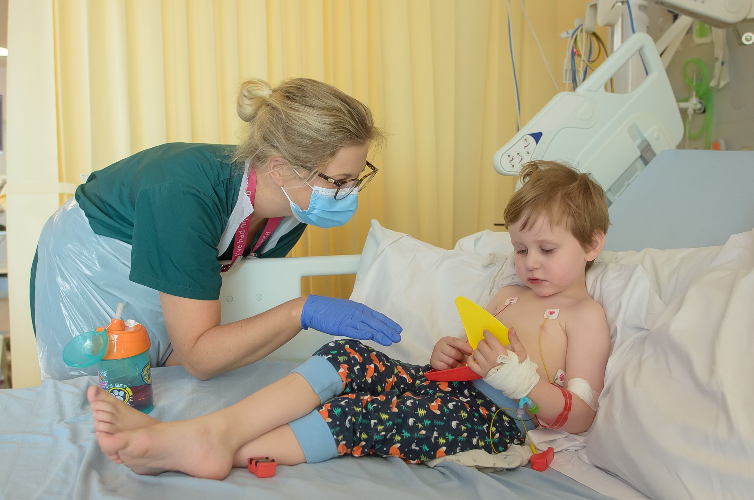 A nurse in PPE talking to a child in a hospital bed